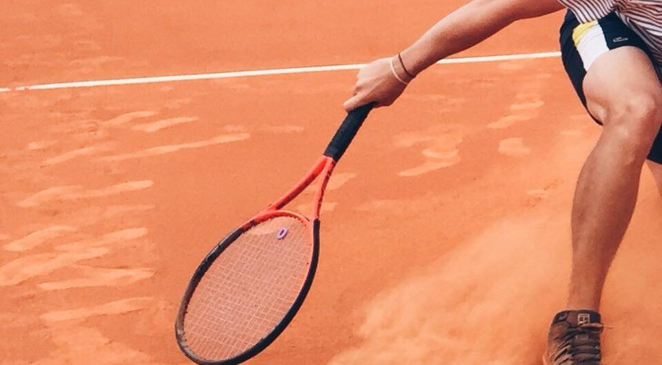 person on clay tennis courts with tennis racket