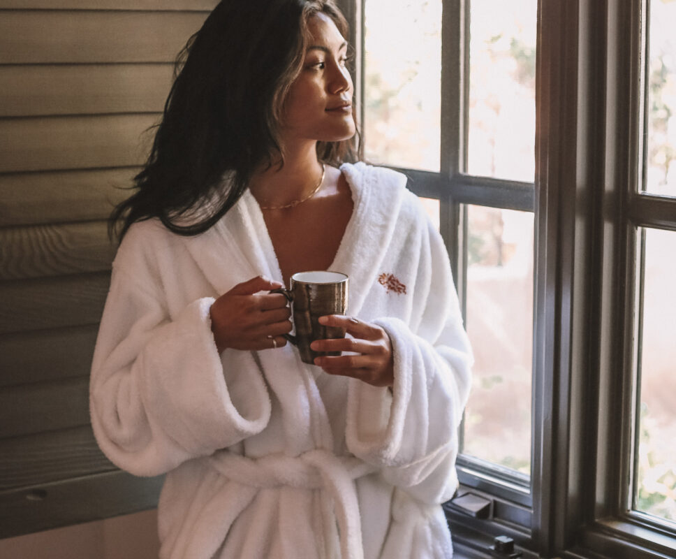 a woman in a robe, drinking tea and gazing out the window of the spa