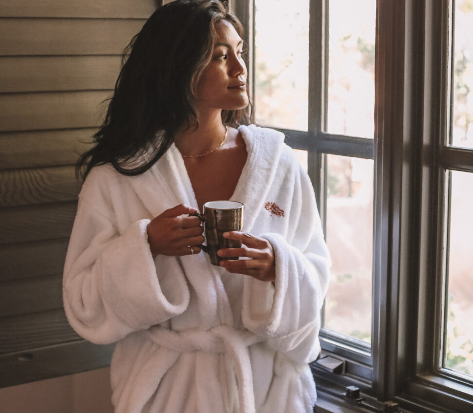 a woman in a robe, drinking tea and gazing out the window of the spa