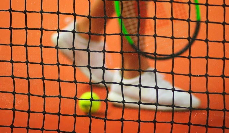 close up of the tennis court net with a players feet in the background