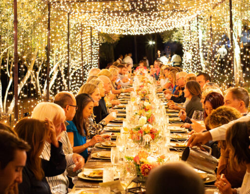 a long dining table full of people with string lights overhead