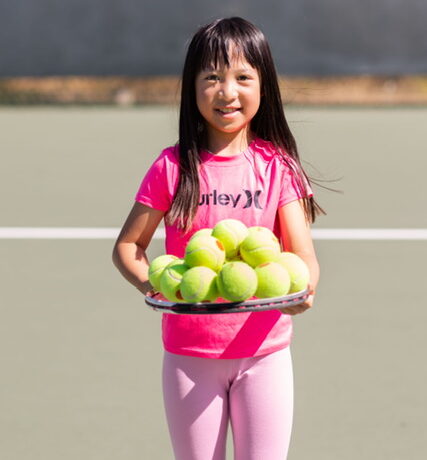 young girl with tennis balls on her racquet